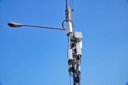 Photo of a streetlamp pole with several cell phone transmitters attached to the top of it. 